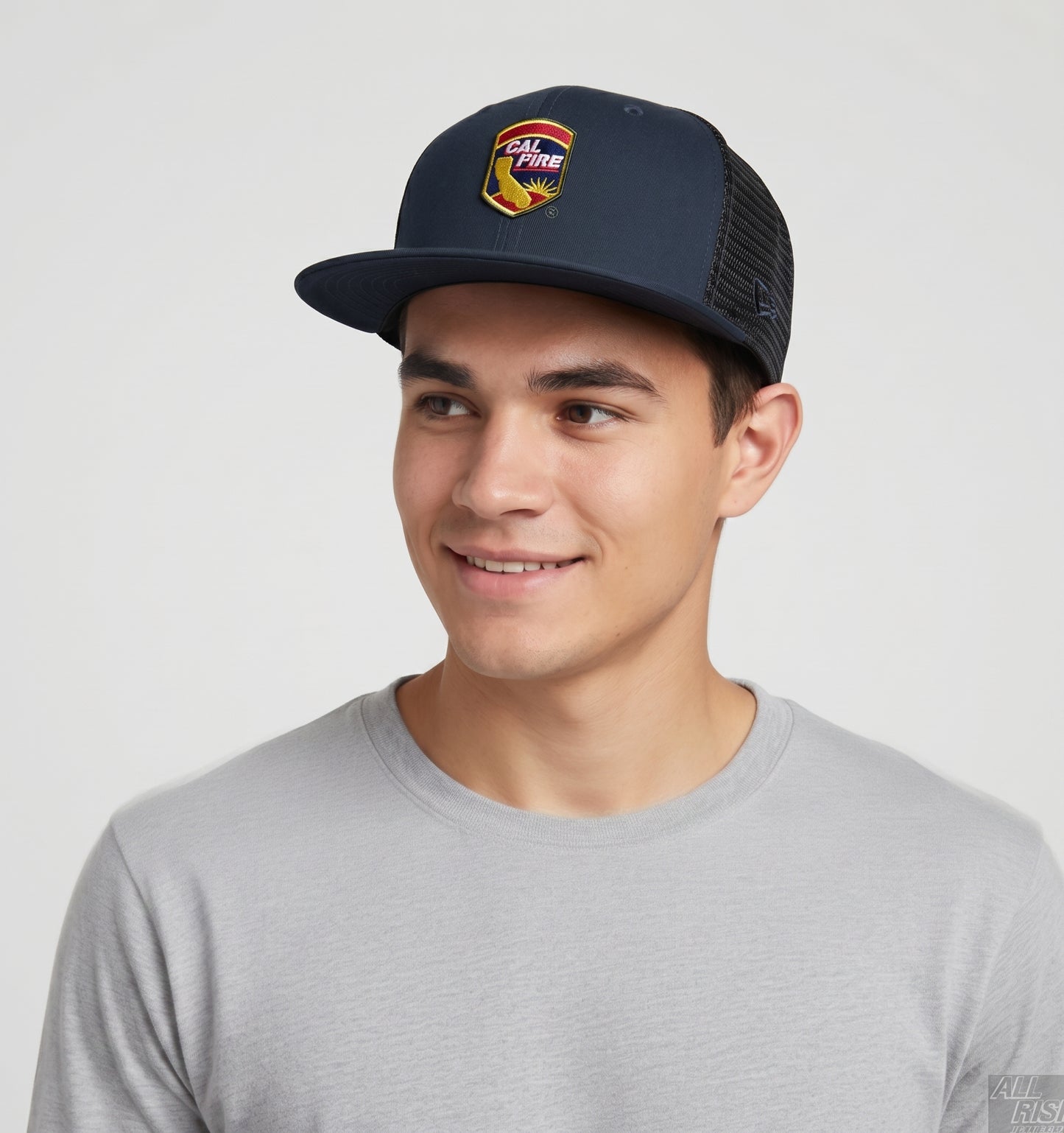 Lifestyle shot of a smiling young man wearing the navy New Era 403 trucker with the colorful CAL FIRE shield crest, flat brim and black mesh back.