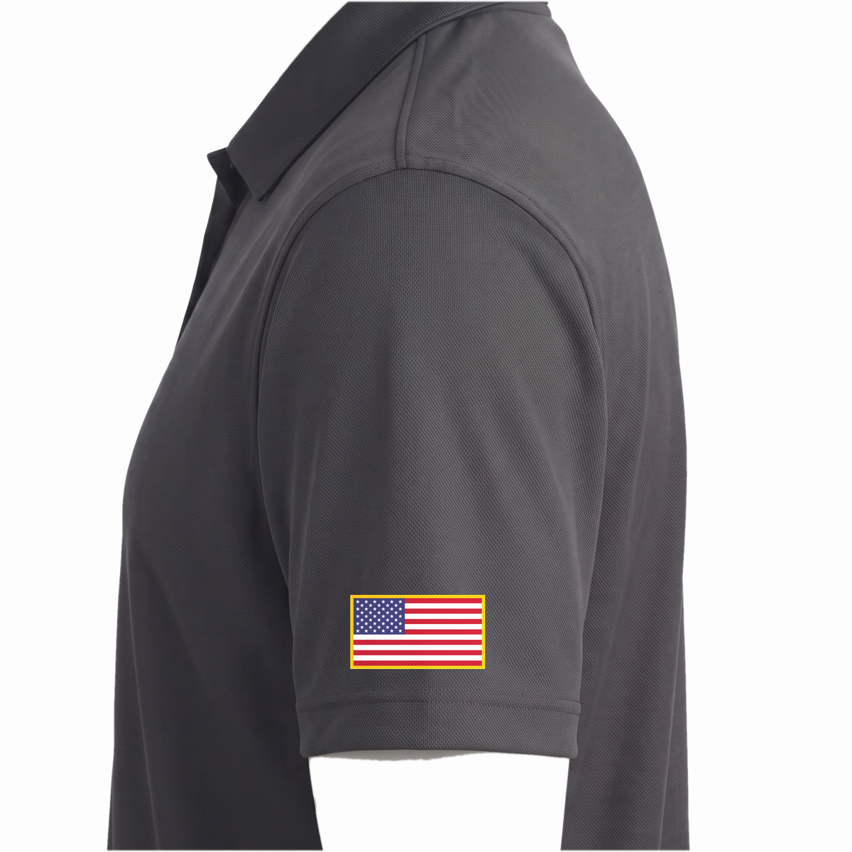 Siskiyou Trojans men's Sport-Tek polo in iron grey, close-up of the left sleeve showing the United States flag patch just above the sleeve hem