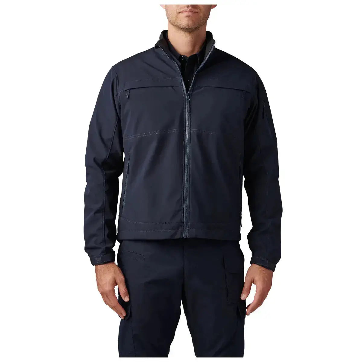 Model wearing the plain navy softshell open over a navy shirt, front view showing the full-zip front, chest yoke seam and zippered hand pockets, no logo.