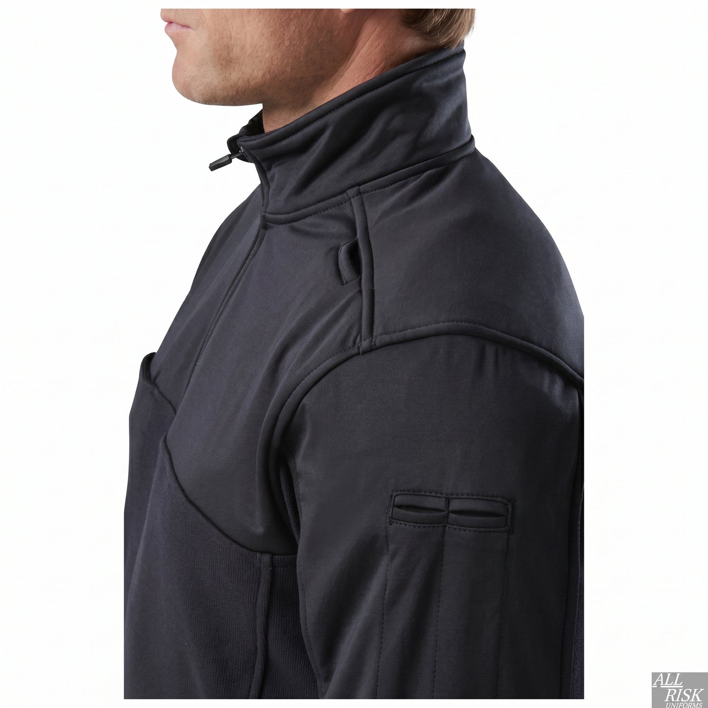 Close-up of the shoulder and collar showing the reinforced shoulder panel, a collar mic loop and a sleeve pocket on the upper arm.