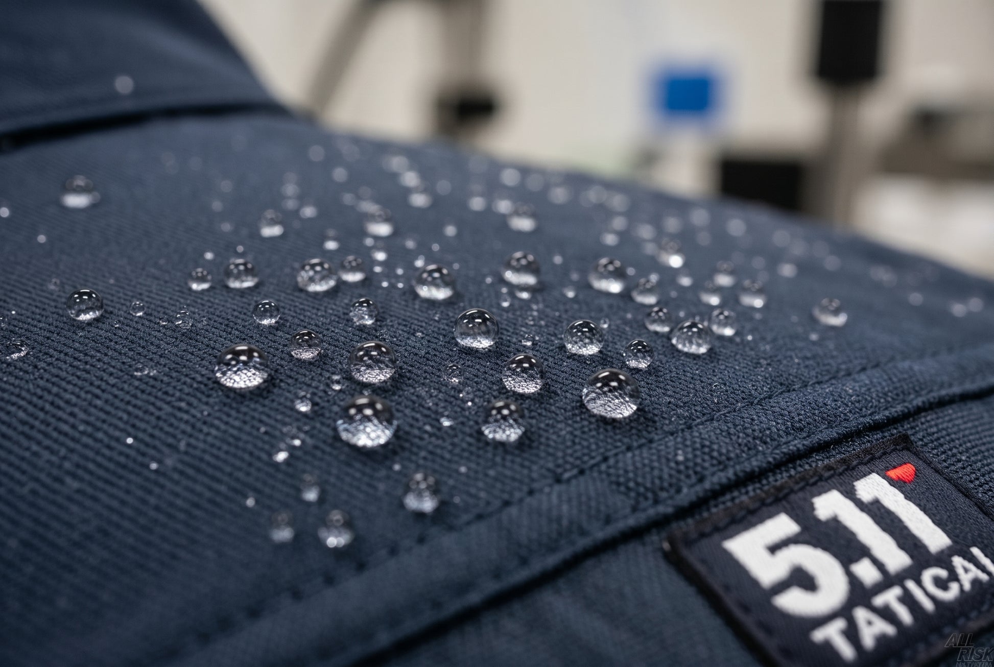 Close-up detail of water beading into droplets on the navy water-repellent fabric, with a small 5.11 Tactical label at the corner.