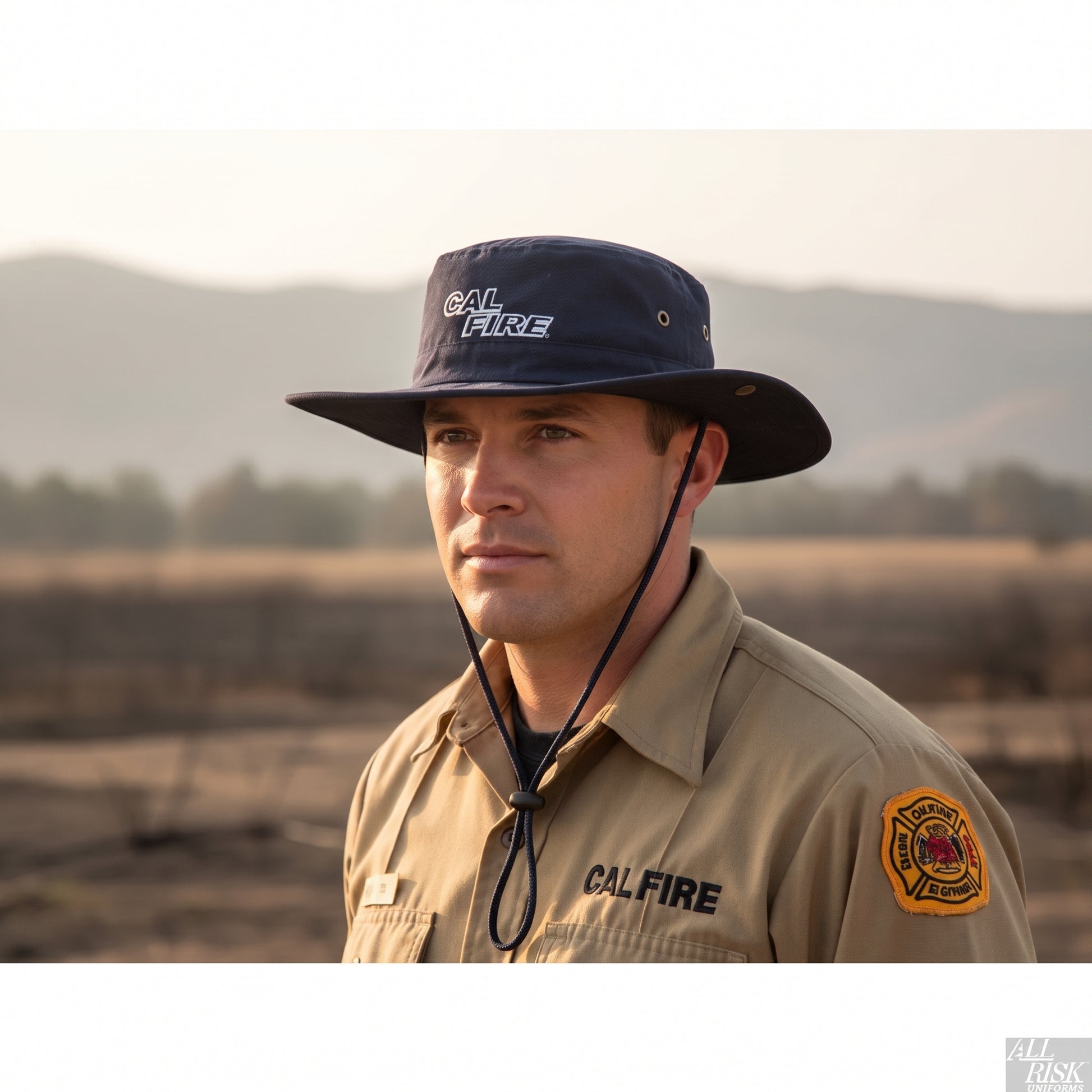 Wildland firefighter in a tan brush shirt on a smoky hillside wearing the navy CAL FIRE Aussie-style boonie hat.