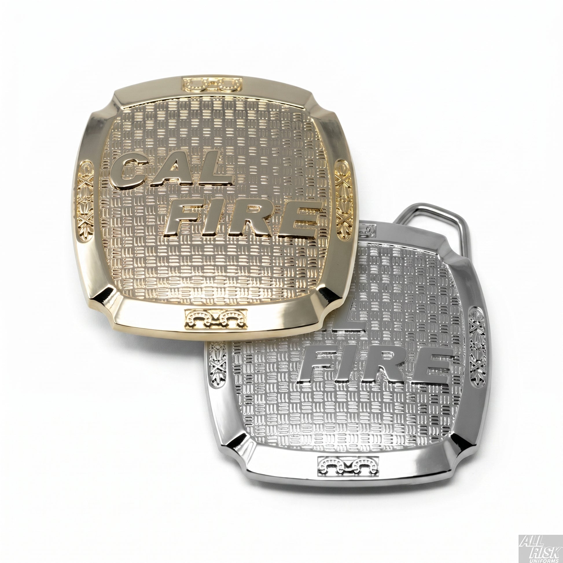 CAL FIRE belt buckle — gold-brass and silver versions side by side, each rectangular cushion shape with raised CAL FIRE serif lettering on a basket-weave-textured center field, decorative scrollwork at the side panels, and small ornamental frames at top and bottom centers.