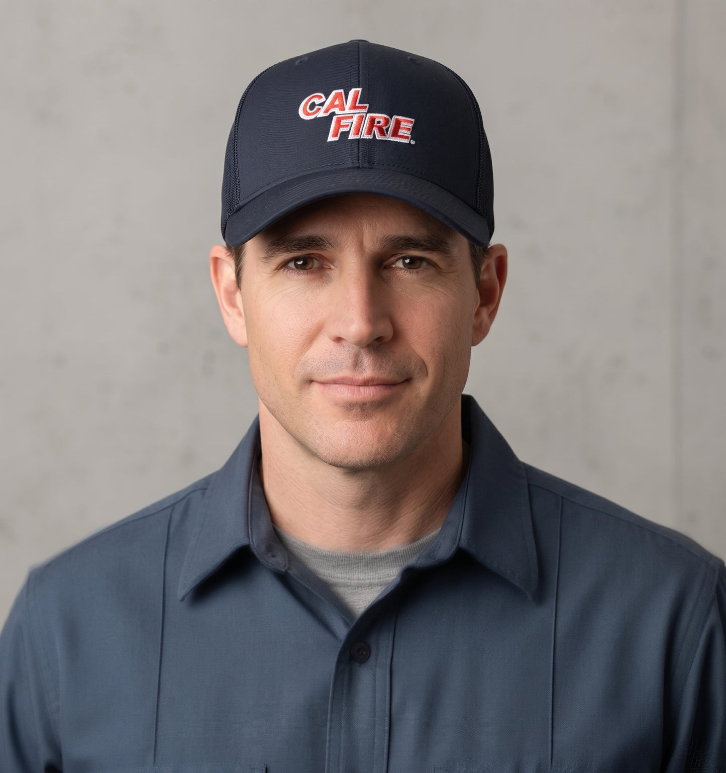 Man in a gray shirt wearing the navy CAL FIRE Flexfit 6511 mesh-back trucker hat with the red wordmark.