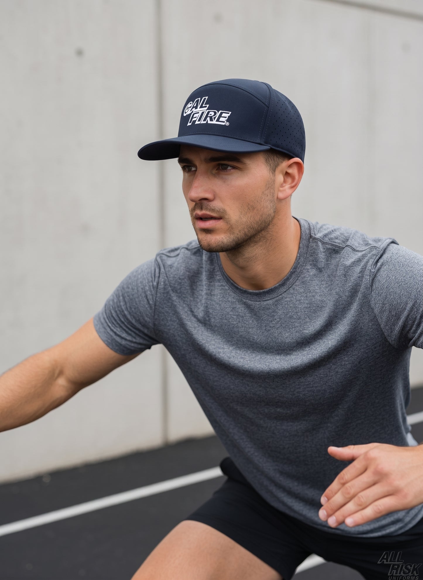 Man in a gray athletic shirt wearing the midnight navy CAL FIRE laser-vented athletic cap with the red wordmark, outdoors.