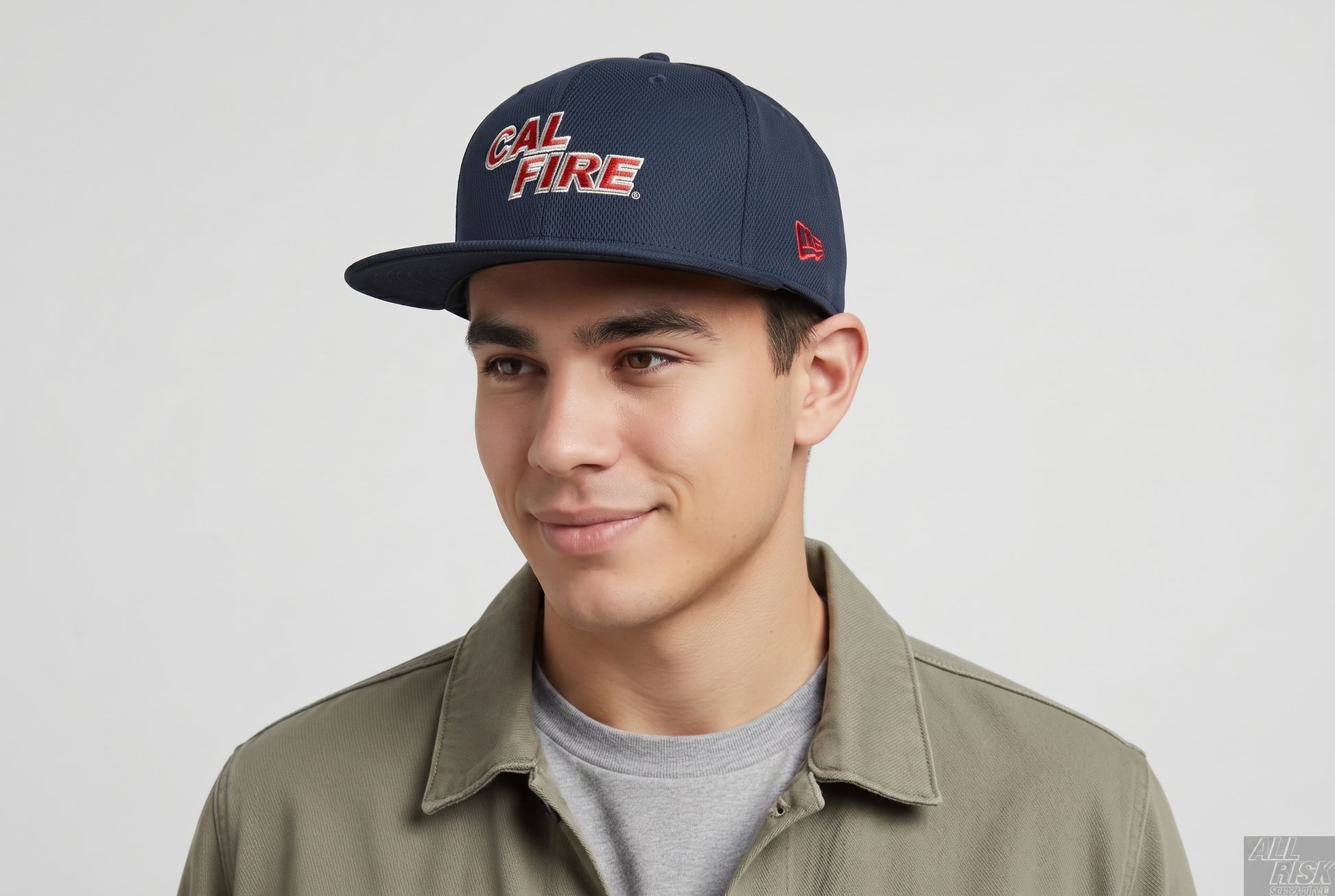 Model close-up of a man in an olive overshirt wearing the navy snapback with the red CAL FIRE wordmark and the New Era flag on the side.