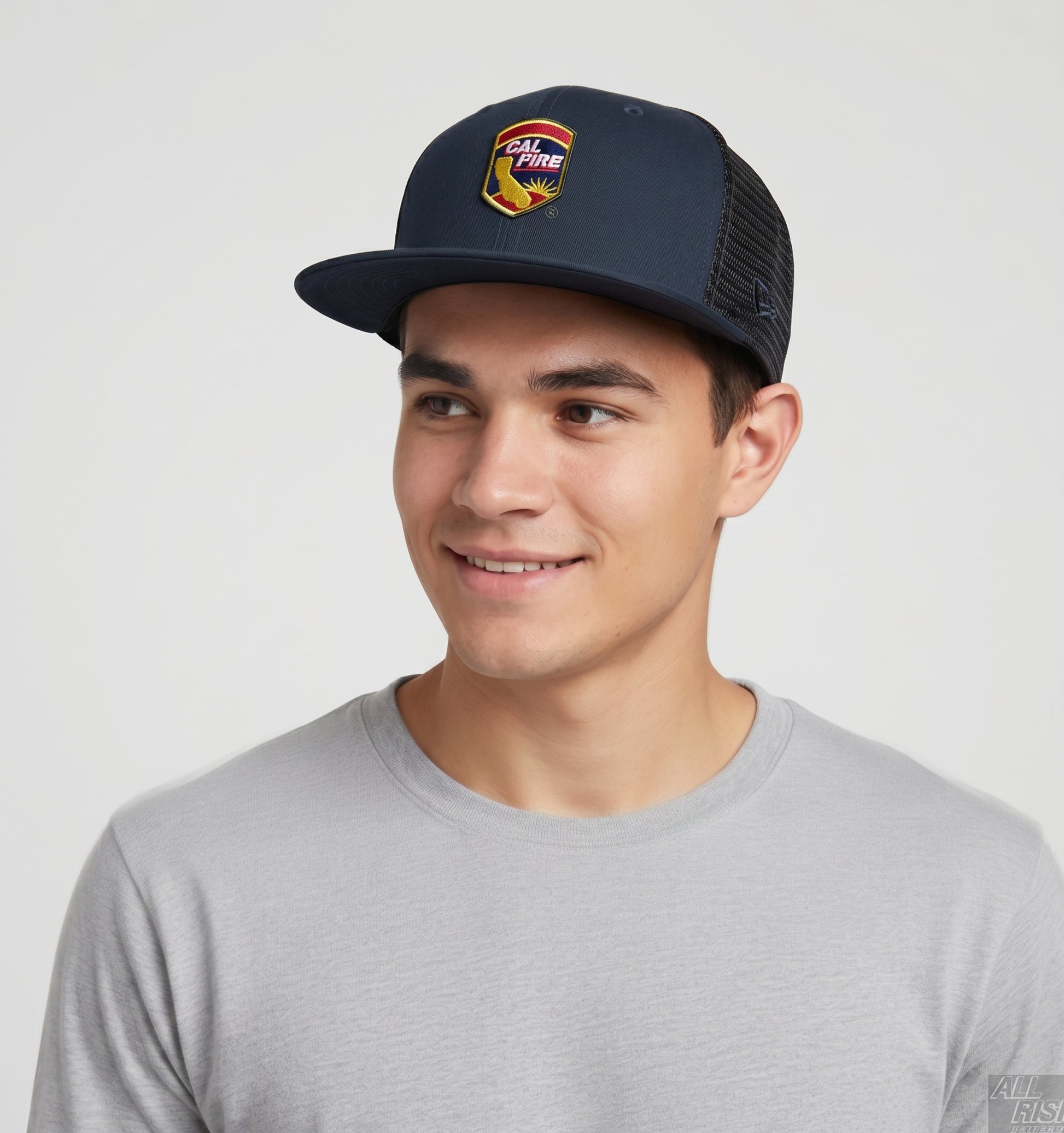 Lifestyle shot of a smiling young man wearing the navy New Era 403 trucker with the colorful CAL FIRE shield crest, flat brim and black mesh back.