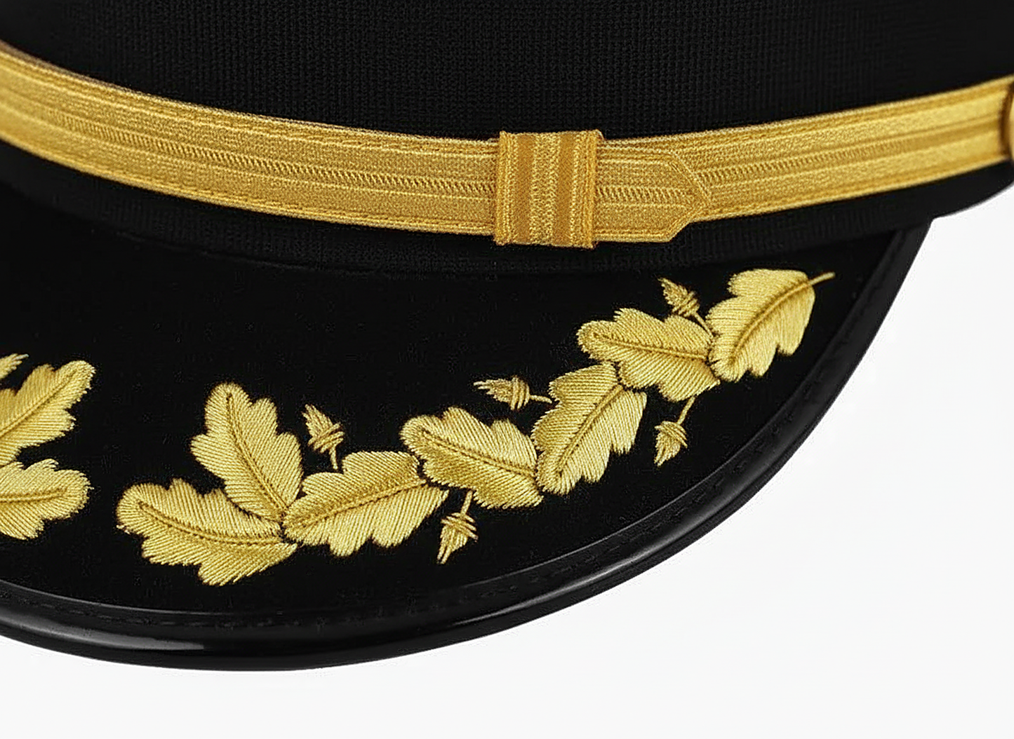 Close-up of the Class A cap visor, showing the gold oak-leaf and acorn embroidery across the black patent-leather brim beneath the gold chin strap.