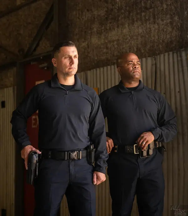 Two men in dark uniforms standing side by side in a dimly lit room.