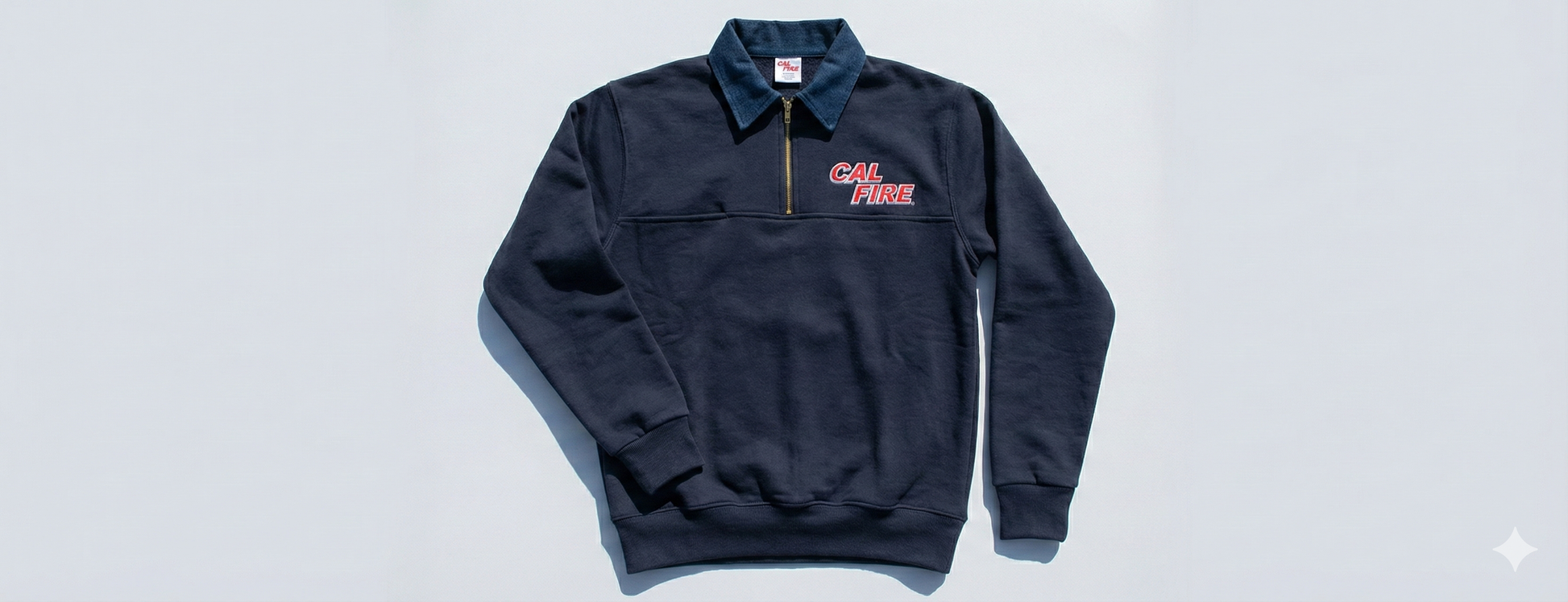 Flat-lay of the navy job shirt on light gray, denim collar and gold zip up top with the small red CAL FIRE wordmark on the chest.